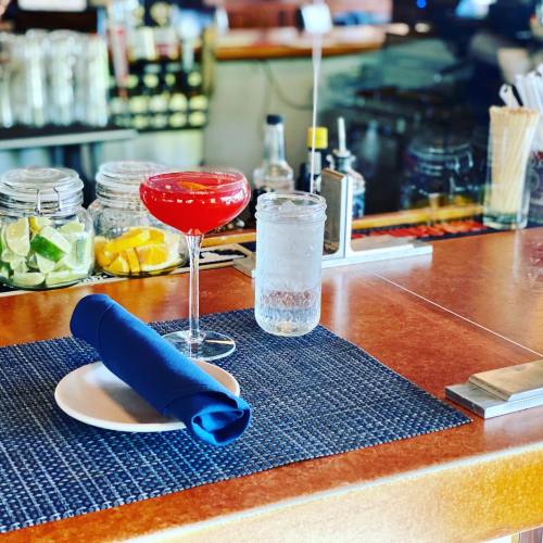 A vibrant red cocktail sits on a bar counter next to a glass of water and a neatly rolled blue napkin.