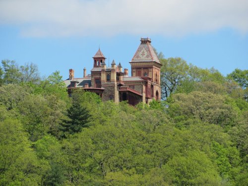 A colorful, ornate castle perched atop a hill, surrounded by lush green trees under a partly cloudy sky.