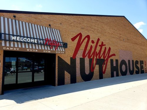 Exterior of Nifty Nut House, featuring a large sign with "Welcome to Nifty Nut House" and colorful murals on the brick wall.