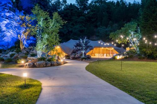 A winding path leads to a tented venue surrounded by trees and illuminated by soft lights in a serene outdoor setting.