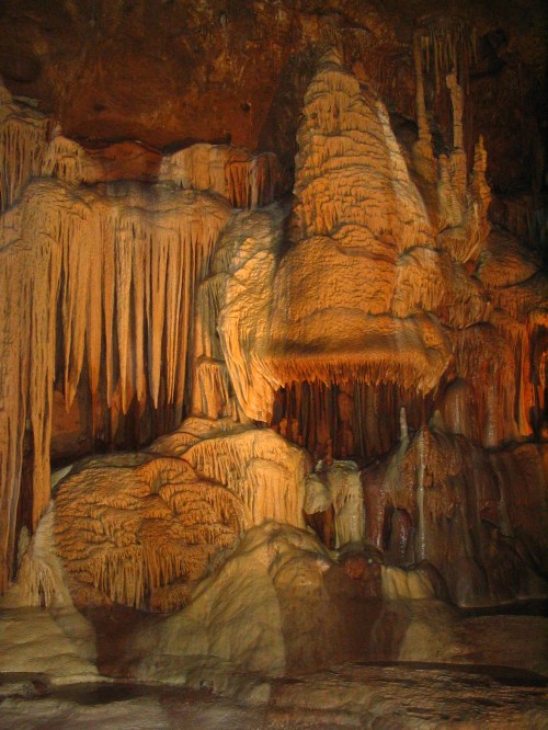 Stalactites and stalagmites in a dimly lit cave, showcasing intricate rock formations and textures.