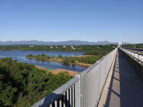 A scenic view from a bridge overlooking a river and lush green landscape with mountains in the background.
