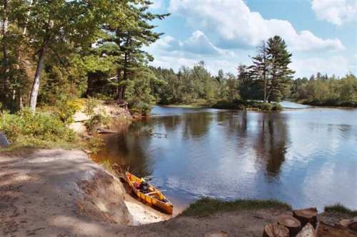 A serene river scene with a kayak on the shore, surrounded by trees and a clear blue sky.