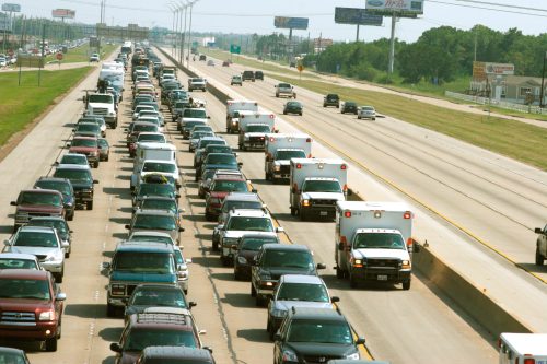 Heavy traffic on a multi-lane highway, with a line of cars and emergency vehicles visible.