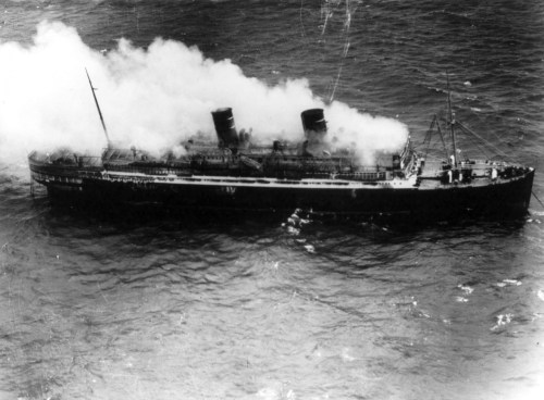 A large ship emits smoke while sailing through rough waters, captured in black and white.