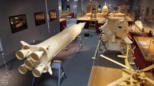 A spacious exhibit featuring intricate wooden models of rockets and spacecraft, with various structures in the background.