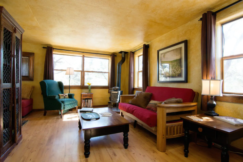 Cozy living room with a green armchair, red futon, wooden coffee table, and large windows letting in natural light.