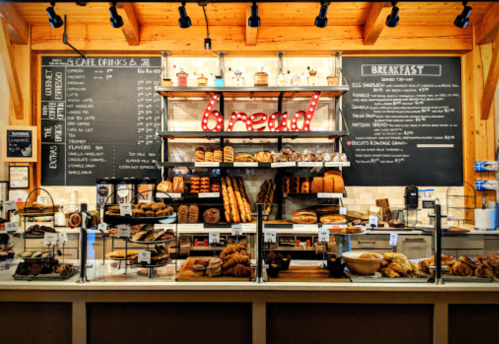 A bakery display featuring various breads and pastries, with a "bread" sign and a menu board in the background.