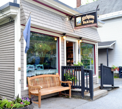 A cozy bakery with a wooden bench outside, featuring a sign that reads "Birchgrove Baking" and a welcoming entrance.