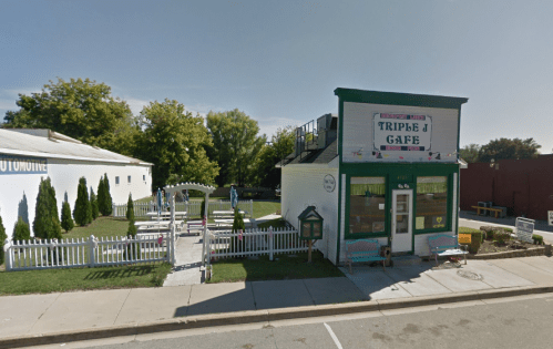 A small café with a green and white exterior, surrounded by a white picket fence and a grassy outdoor seating area.