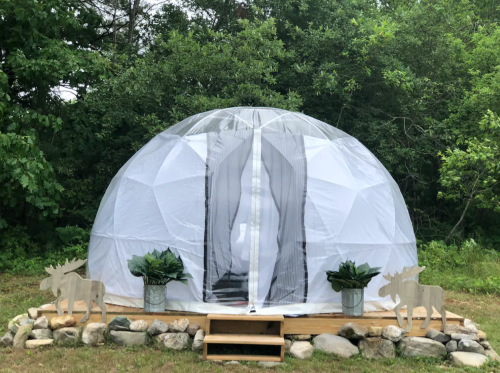 A geodesic dome structure with a clear entrance, surrounded by greenery and stone landscaping.