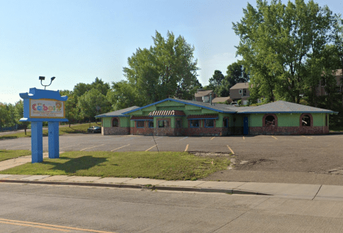 A colorful restaurant building with a sign, surrounded by trees and an empty parking lot.