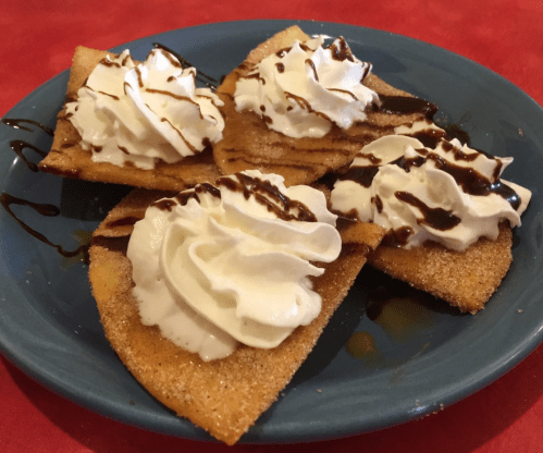 A blue plate with four crispy dessert triangles topped with whipped cream and drizzled with chocolate sauce.
