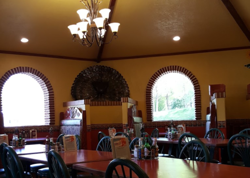 Interior of a restaurant featuring colorful walls, arched windows, and wooden tables with chairs.