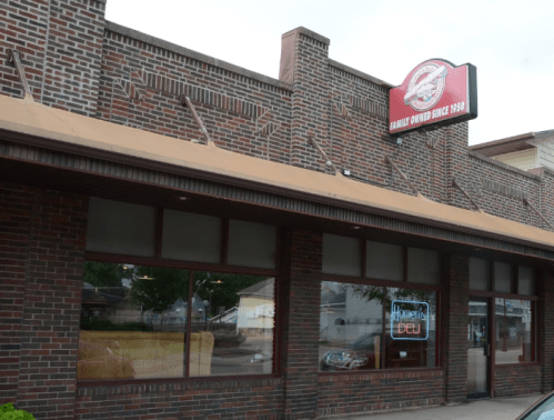 Exterior of a brick building with a sign reading "Family Owned Since 1969" and a neon "Deli" sign in the window.