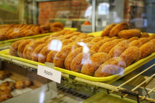 A display case filled with freshly made apple donuts, arranged neatly on a yellow tray.