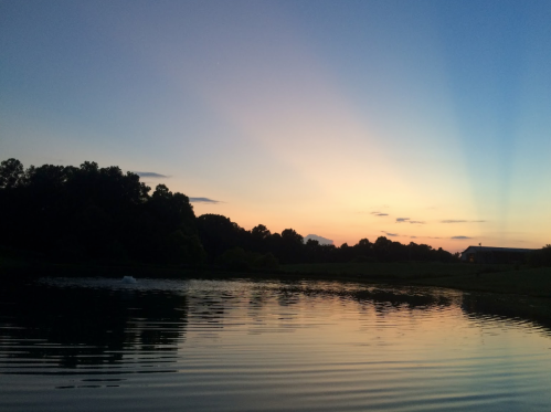 A serene sunset over a calm lake, with colorful sky reflections and silhouettes of trees in the background.