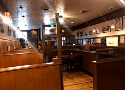 Interior of a cozy restaurant with wooden booths, warm lighting, and vintage decor. A staff member is seen in the background.