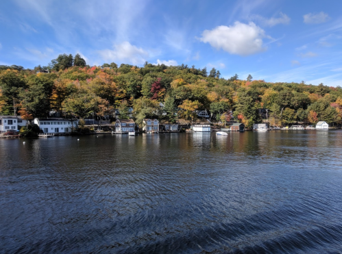 A serene lake scene with colorful autumn foliage and charming houses along the shore under a blue sky.