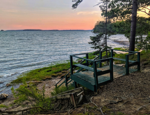 A wooden deck by the water at sunset, surrounded by trees and a calm lake with gentle waves.