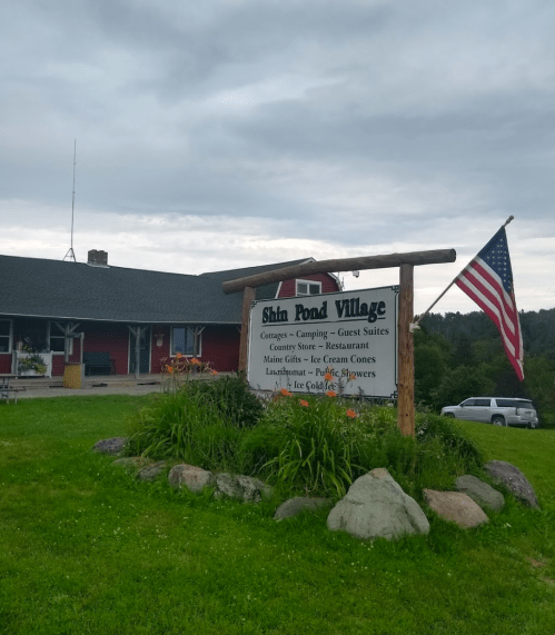 Sign for Shin Pond Village with American flag, featuring cottages, camping, a restaurant, and a country store.
