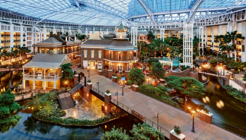 A spacious indoor atrium featuring lush greenery, water features, and elegant architecture under a glass roof.