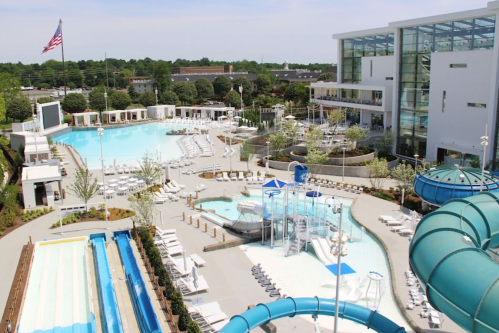 Aerial view of a large outdoor pool area with slides, lounge chairs, and a modern building in the background.