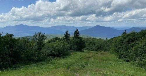 A scenic view of rolling mountains under a partly cloudy sky, with lush greenery in the foreground.