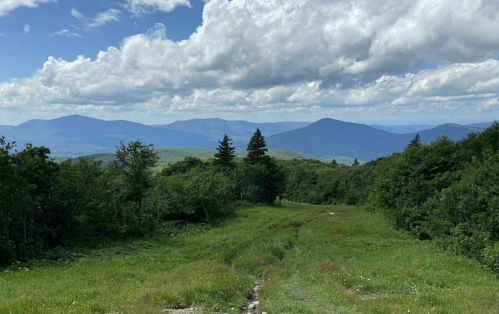 A scenic view of rolling green hills and mountains under a partly cloudy sky.