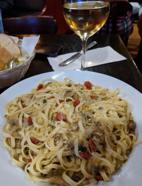 A plate of fettuccine pasta with sun-dried tomatoes and a glass of white wine on a table.