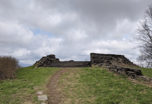 Ruins of stone steps leading up a grassy hill under a cloudy sky.