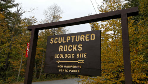 Sign for Sculptured Rocks Geologic Site in New Hampshire, surrounded by autumn foliage.