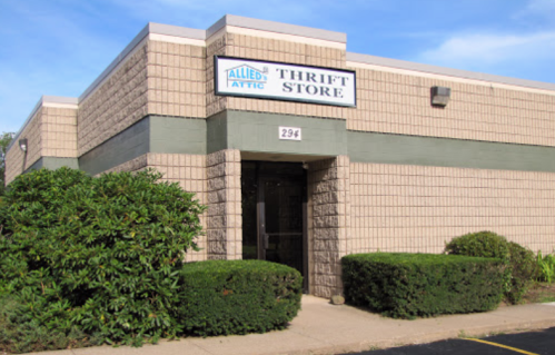 Exterior of a thrift store building with a sign that reads "Allied Attic Thrift Store" and neatly trimmed bushes.