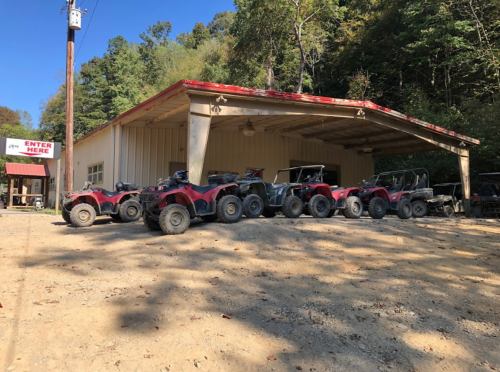 A row of ATVs parked outside a building in a wooded area, with a sign that says "ENTER HERE."