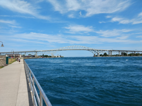 A wide view of a bridge over a blue river, with a clear sky and a walkway along the water's edge.