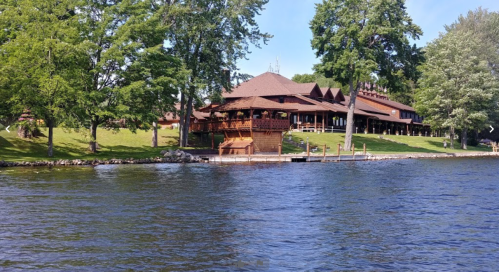 A wooden lodge by a lake, surrounded by green trees and a clear blue sky.