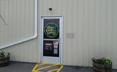 Entrance to Blue Earl Brewing, featuring a round sign and an "Open" notice on the door. Planters are on either side.