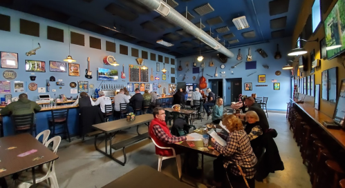 A lively bar with patrons seated at tables and the bar, decorated with guitars and music-themed art on the walls.