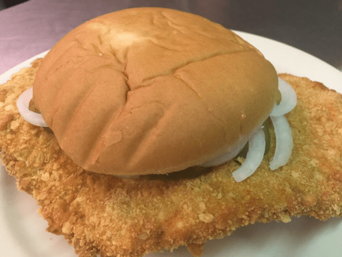 A crispy fried chicken sandwich with a soft bun and sliced onions on a white plate.