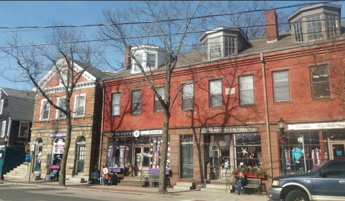 A row of brick buildings with shops, trees bare of leaves, and a clear blue sky in the background.