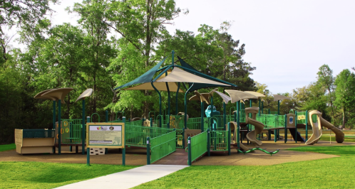 A colorful playground with slides and climbing structures, surrounded by trees and green grass.