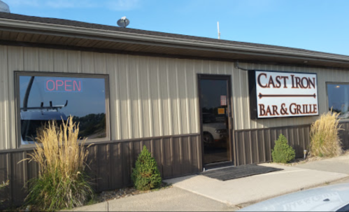 Exterior of Cast Iron Bar & Grille with "OPEN" sign, featuring a metal facade and landscaping in front.
