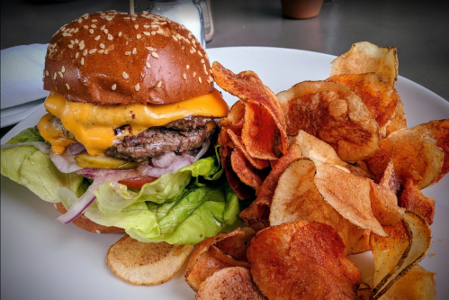 A juicy cheeseburger with lettuce, tomato, and onion, served with a side of crispy potato chips on a white plate.