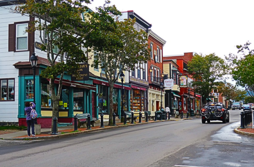 A charming street lined with colorful shops and trees, featuring a vintage car parked along the curb.