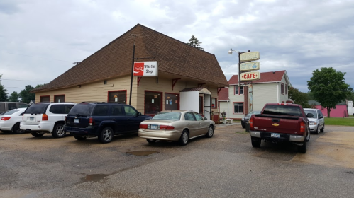A small, rustic building with a sign reading "Whistle Stop" and several parked cars in front. Overcast sky.