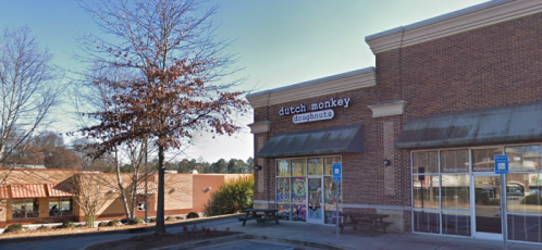 Exterior of Dutch Monkey Doughnuts shop with a parking lot and nearby buildings on a clear day.