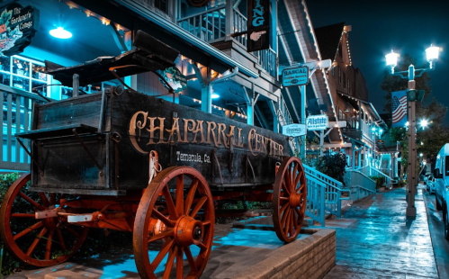 A vintage wagon with "Chaparral Center" signage parked on a lit street, surrounded by charming buildings at night.
