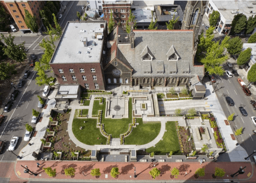Aerial view of a landscaped area featuring a church and surrounding buildings in an urban setting.