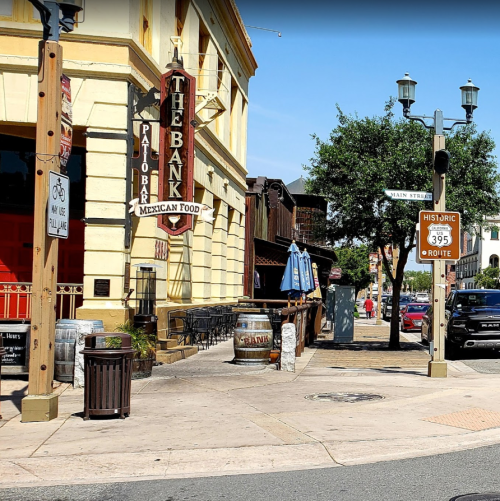 A street view featuring a restaurant sign, outdoor seating, and historic route markers in a sunny urban setting.