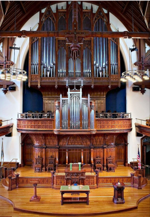 Interior of a grand church featuring a large wooden altar, intricate carvings, and a prominent pipe organ.